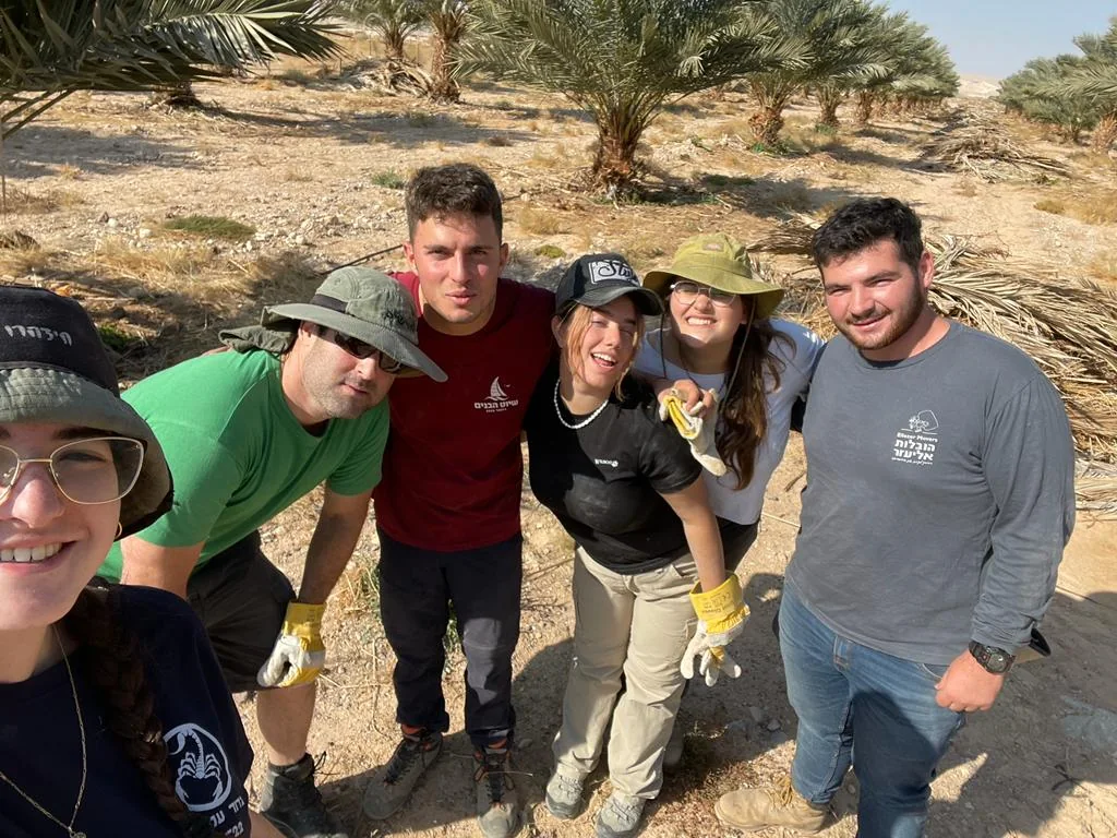 קבוצה מחייכת מתחת לדקלים במטע
