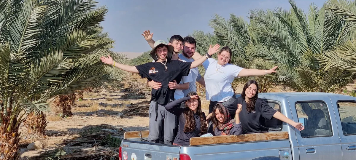 קבוצה מצטלמת בארגז טנדר בין הדקלים