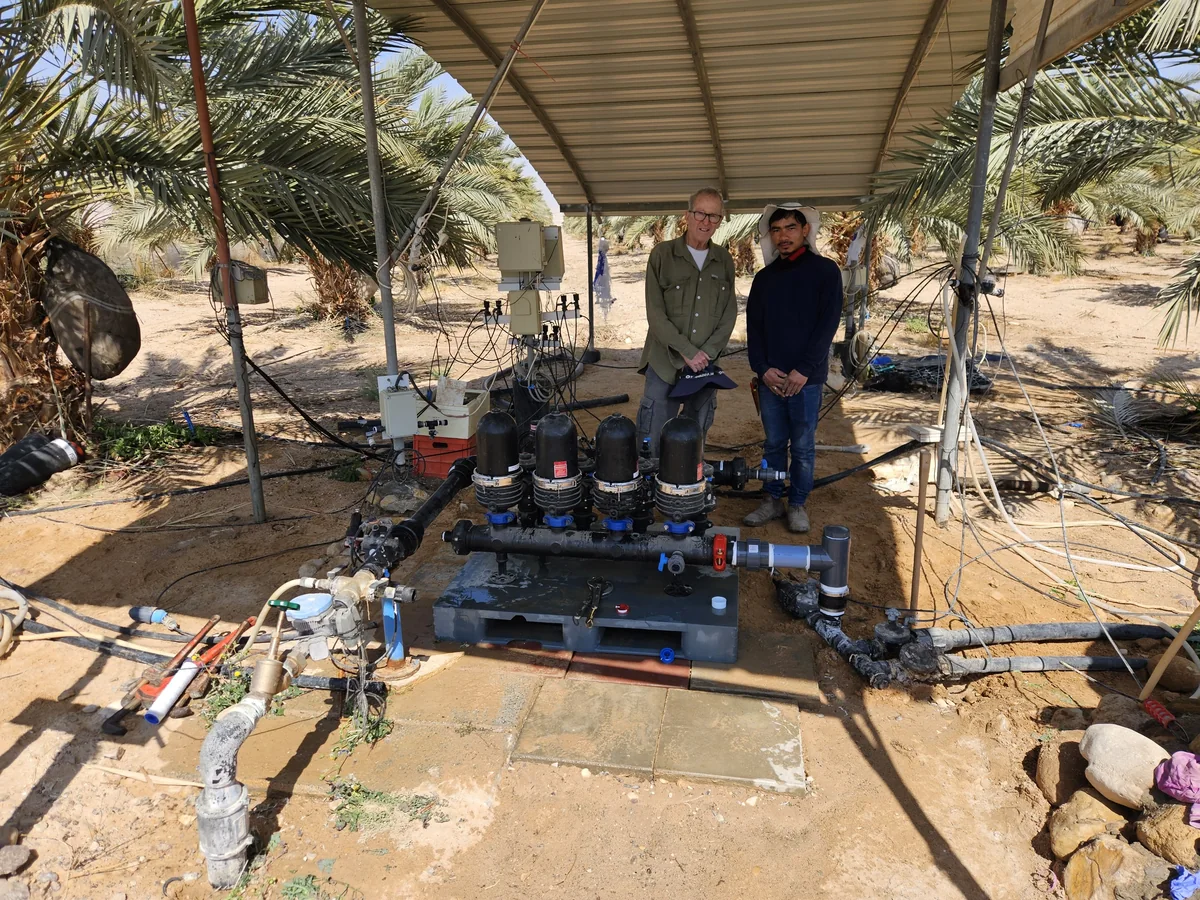 אנשים לצד צינורות וברזים במערכת ההשקיה במטע